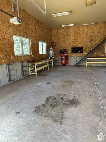 Concrete flooring with overhead fluorescent lighting, exposed plywood walls, and multiple windows