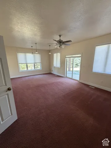 Spacious room with multiple windows, a ceiling fan, and pendant lighting