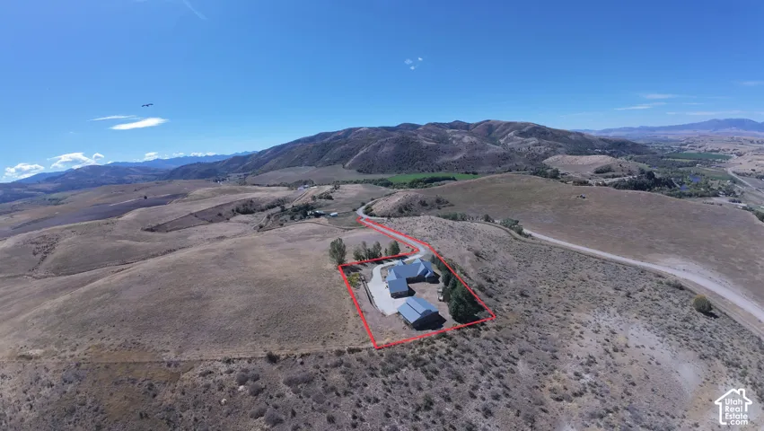 Aerial perspective of property featuring a multi-structure residence, paved driveway, mature trees, and expansive topography