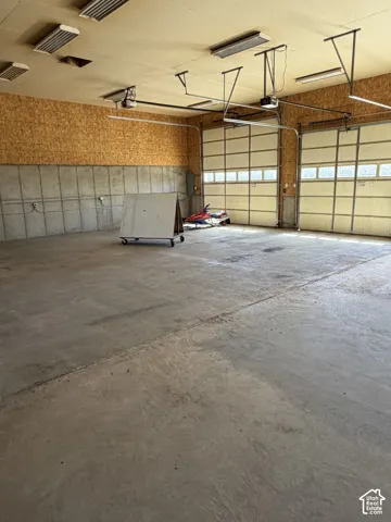Spacious garage featuring two overhead doors, concrete flooring, exposed plywood walls, and overhead fluorescent lighting