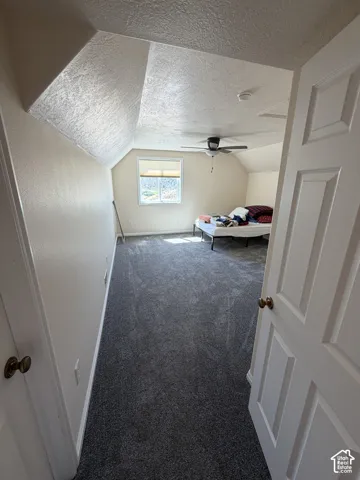 Spacious room featuring textured vaulted ceilings, plush gray carpeting, a ceiling fan, and an operable window