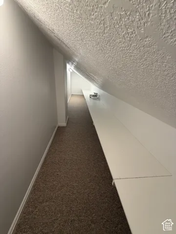 Sloped ceiling with textured finish, built-in shelving, and recessed lighting