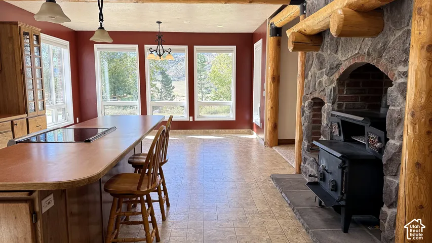 Kitchen area featuring a wood-topped center island with a built-in cooktop, fieldstone fireplace with an integrated metal stove, rustic log pillars, and large picture windows