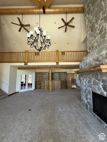 Vaulted ceiling with exposed wood beams, stone-clad fireplace, integrated wood shelving and cabinetry, and a second-story open-rail balcony
