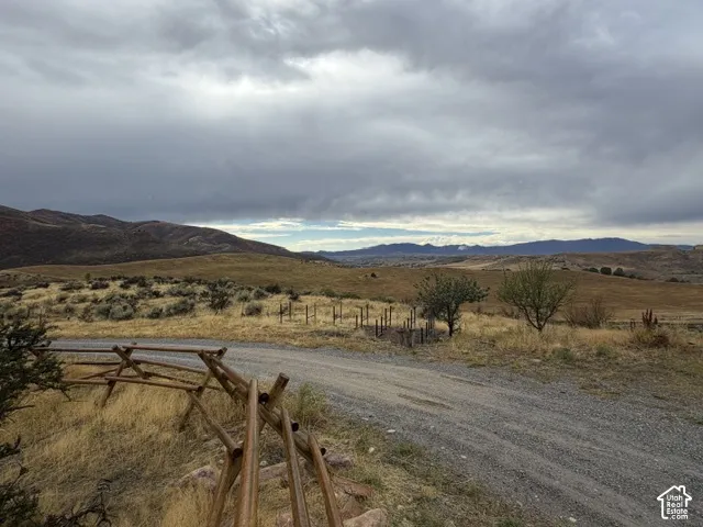 Gravel driveway with a split rail fence, expansive open terrain, and distant mountain ranges