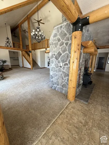 Vaulted ceilings with exposed wood beams, a stone-clad fireplace with a wood-burning stove, and a grand staircase with wood railings