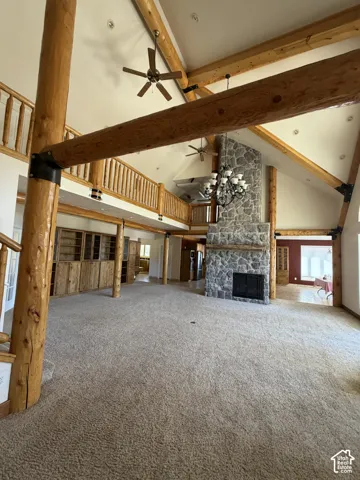 Vaulted ceiling with exposed wood beams, stone fireplace, built-in wooden cabinetry, and an upper-level balcony