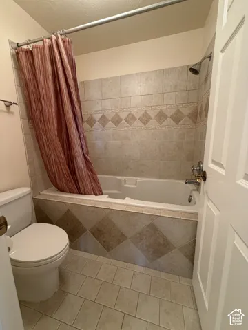 Bathtub with tiled surround, shower fixture, tiled flooring, and a toilet