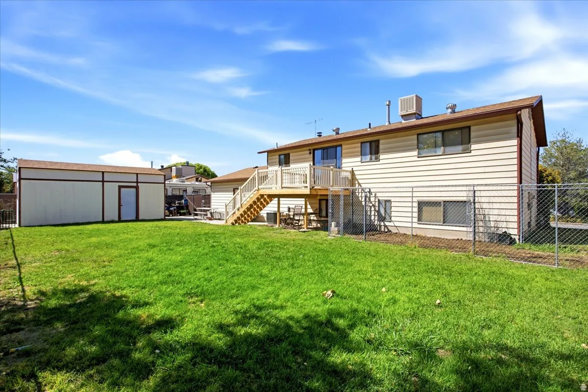 Expansive backyard with a manicured lawn, a detached storage building, and a raised wooden deck with staircase