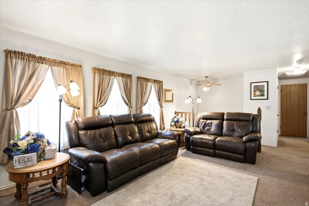 Living area featuring carpet flooring, multiple windows with drapes, and a ceiling fan