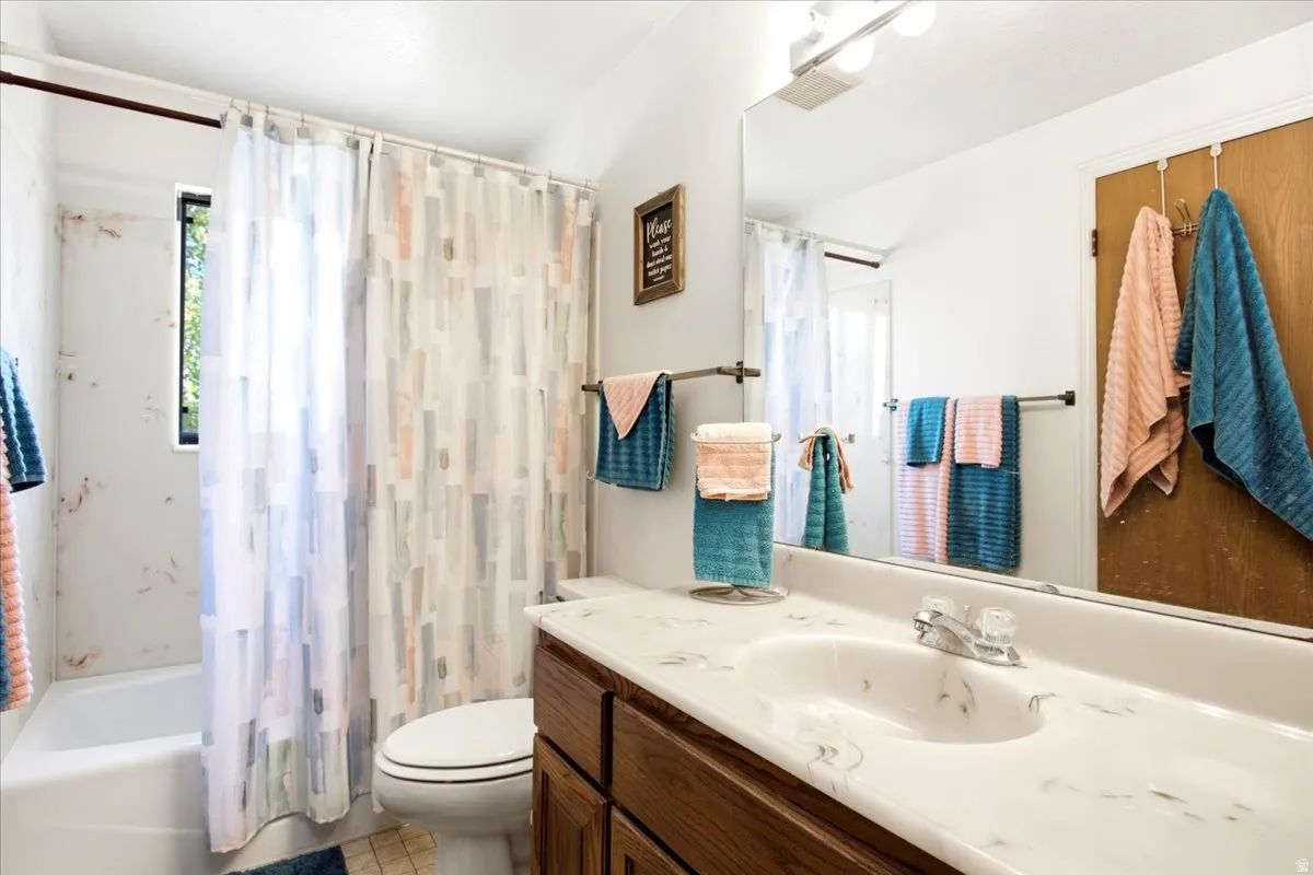 Bathroom featuring a single vanity with wood-finish cabinetry, a single basin sink, a large wall-mounted mirror, and a combined shower and tub with a window