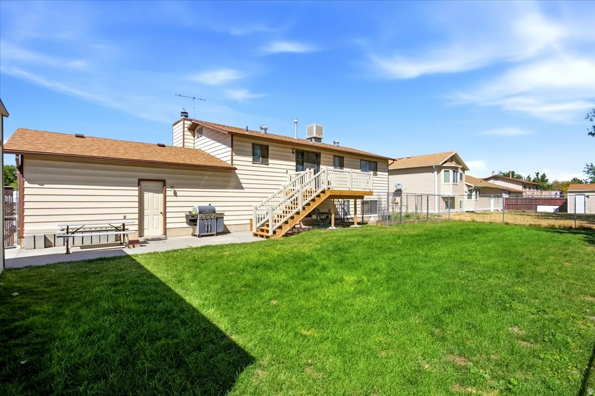 Expansive green lawn with a wood deck, wood staircase, and an attached storage structure