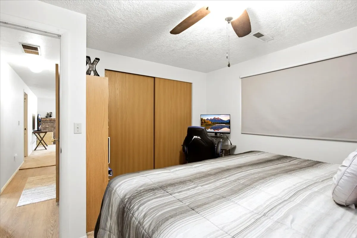Bedroom featuring a ceiling fan with integrated lighting, wood-finish sliding closet doors, and light-filtering window treatments