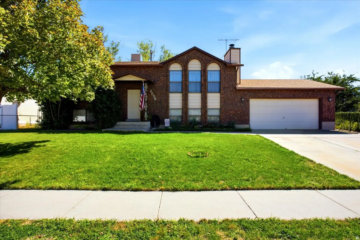 Brick exterior with arched windows, attached garage, concrete driveway, and mature landscaping