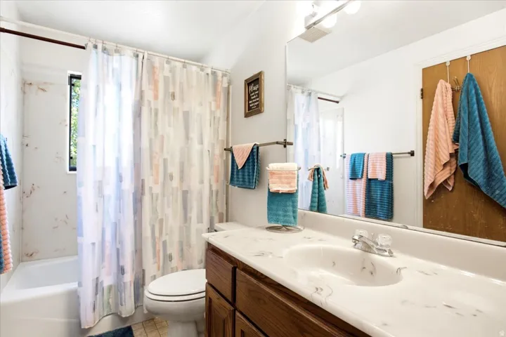 Bathroom featuring a single vanity with wood-finish cabinetry, a single basin sink, a large wall-mounted mirror, and a combined shower and tub with a window
