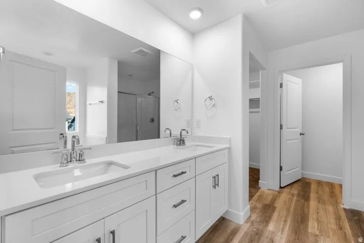Dual vanity with integrated sinks, white cabinetry, chrome fixtures, and wood-finish flooring