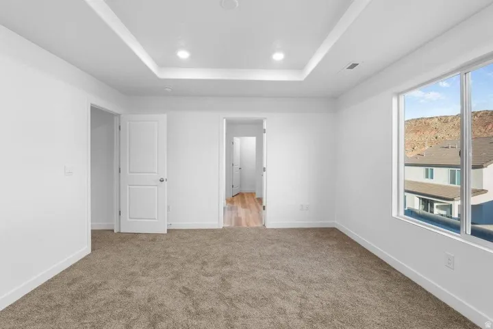 Recessed tray ceiling with integrated lighting, expansive window, neutral tone carpeting, and white trim