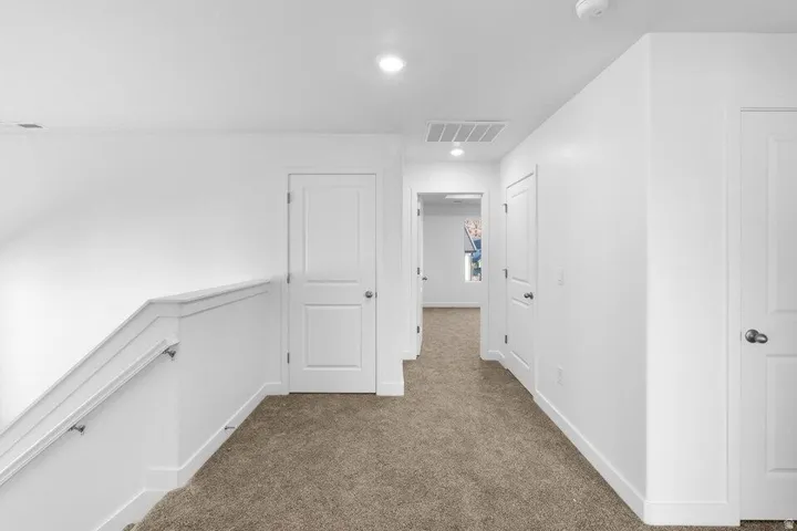 Carpeted hallway with white walls and recessed lighting
