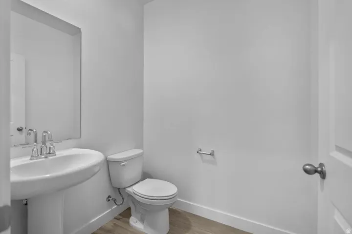 Pedestal sink with chrome fixtures, elongated toilet, rectangular wall mirror, and wood-finish flooring