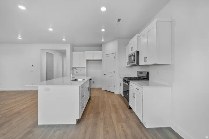 Modern kitchen featuring light wood-finish flooring, white cabinetry, integrated stainless steel appliances, a center island with a sink, and recessed lighting
