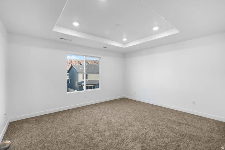 Recessed lighting within a tray ceiling, carpeted flooring, and a window offering a distant mountain backdrop