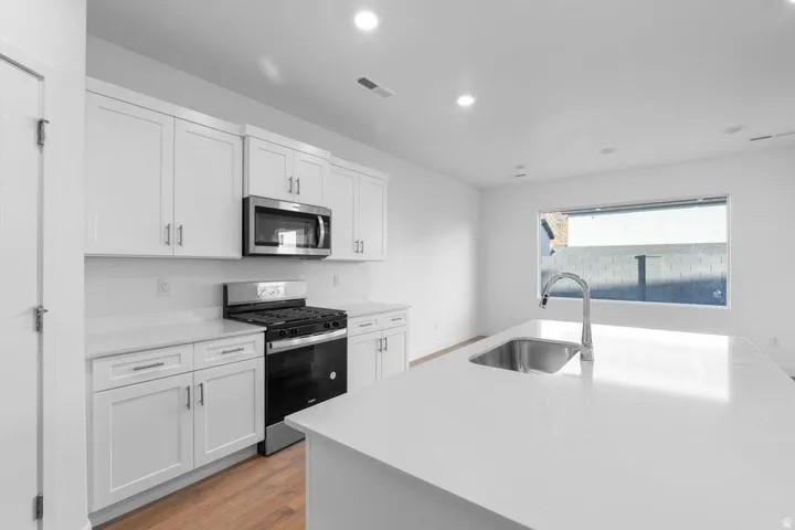 White shaker cabinetry, stainless steel appliances, central island with undermount sink, recessed lighting, and wood-finish flooring