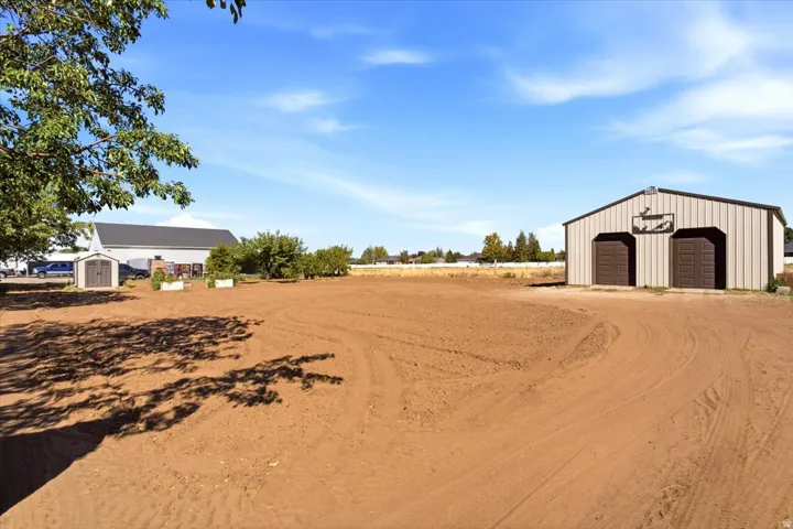 Metal barn with two roll-up doors, an open field, and an additional shed