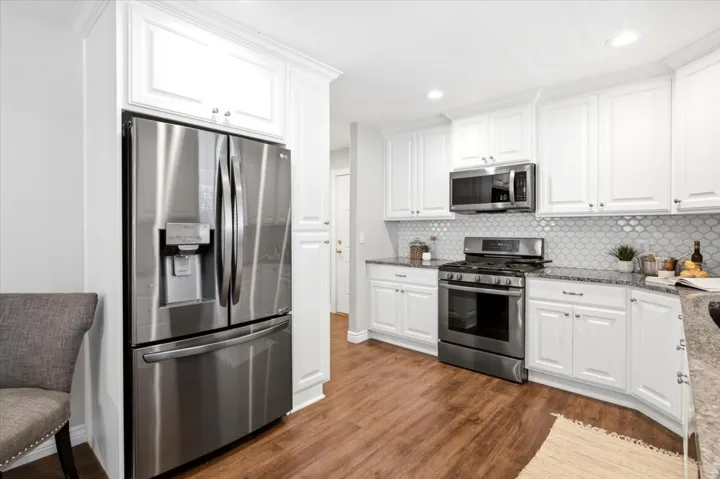 Full-sized stainless steel refrigerator, white shaker-style cabinetry, mosaic tile backsplash, stainless steel range with microwave, and wood-finish flooring
