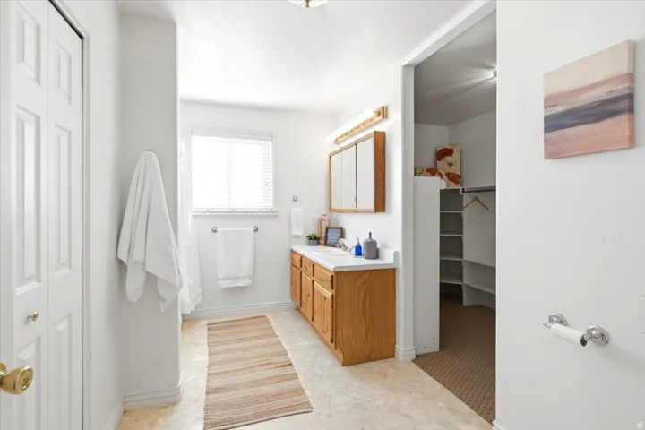 Bathroom featuring a double vanity with wood cabinetry, a window with blinds, and a built-in closet with shelving and a hanging rod