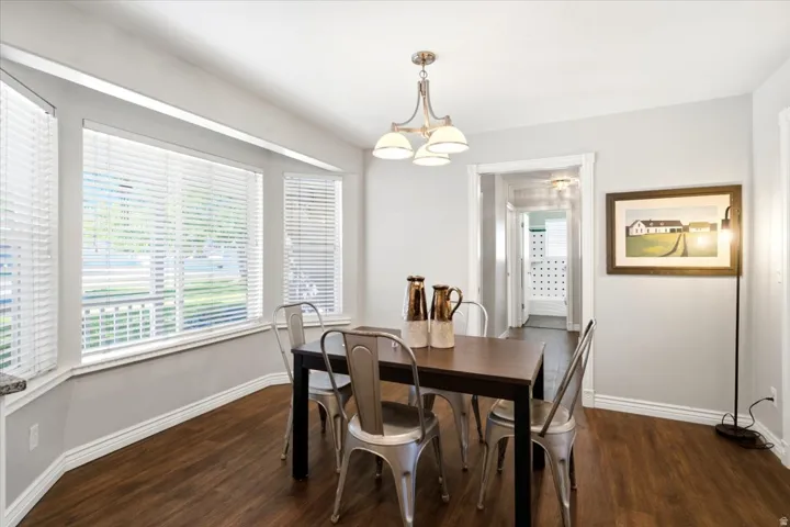 Bay window with white blinds, wood-finish flooring, white trim, and a decorative pendant light fixture