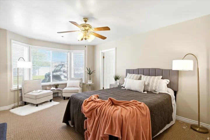 Recessed bay window with blinds, ceiling fan with integrated lighting, and neutral carpeting