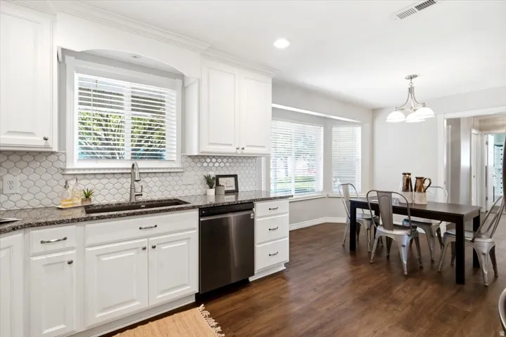 White cabinetry, stone countertops, stainless steel dishwasher, wood-finish flooring, and a bay window