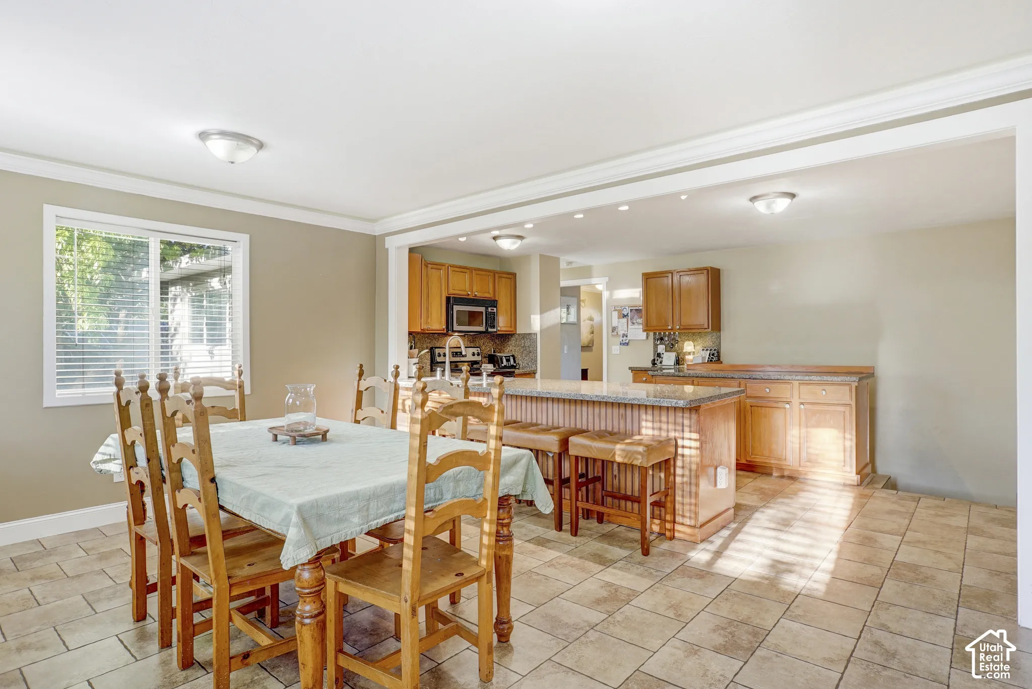 Open-concept dining and kitchen area with tile flooring, a kitchen island with stone countertop, and wood cabinetry