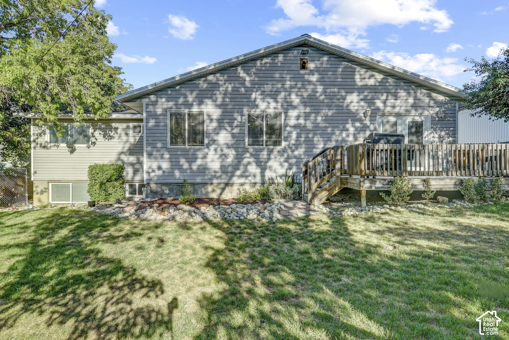 Expansive rear lawn, multi-level wood deck, gray horizontal siding, multiple windows, and a landscaped rock feature