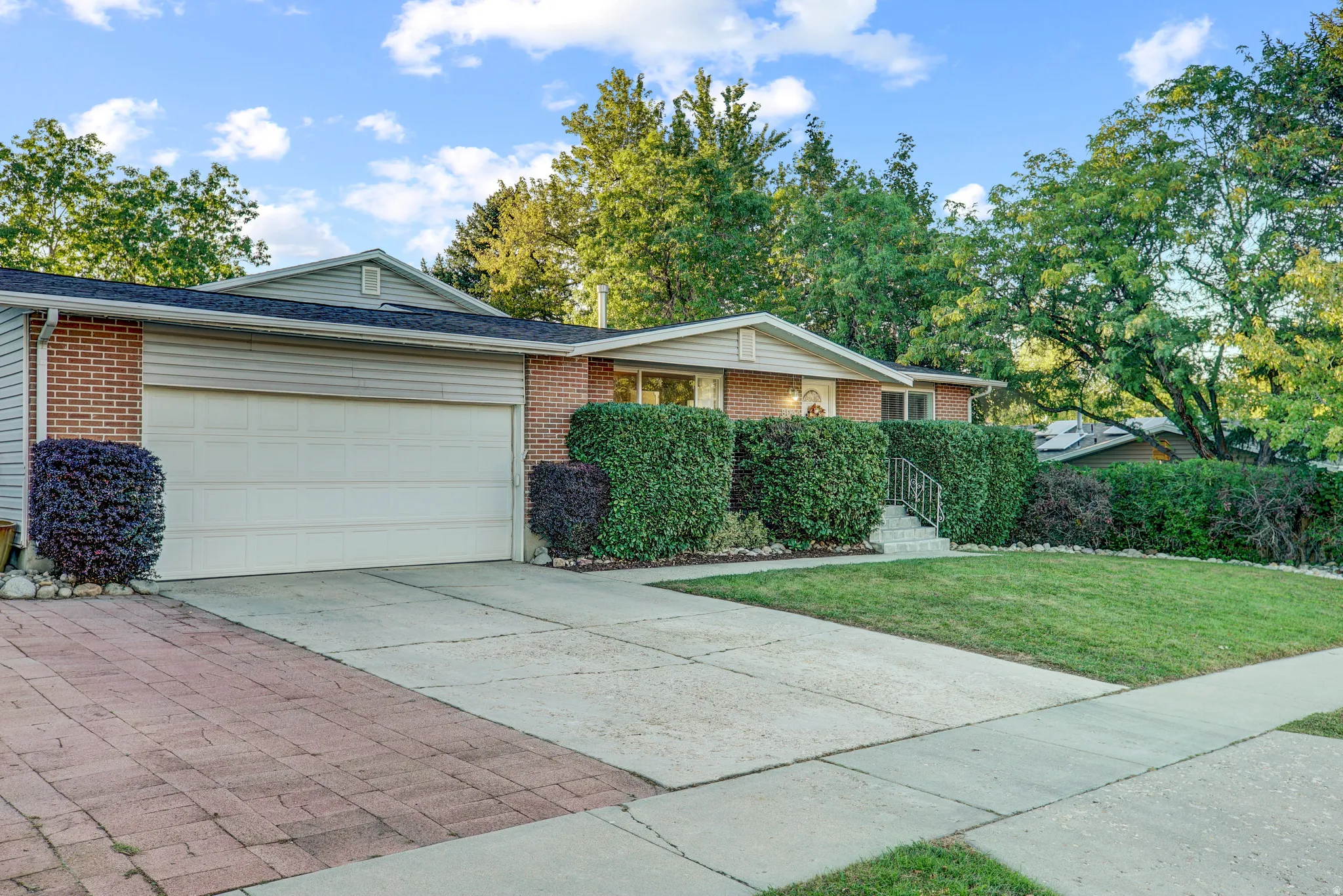 Brick exterior, attached garage, concrete driveway, paver stone section, mature landscaping