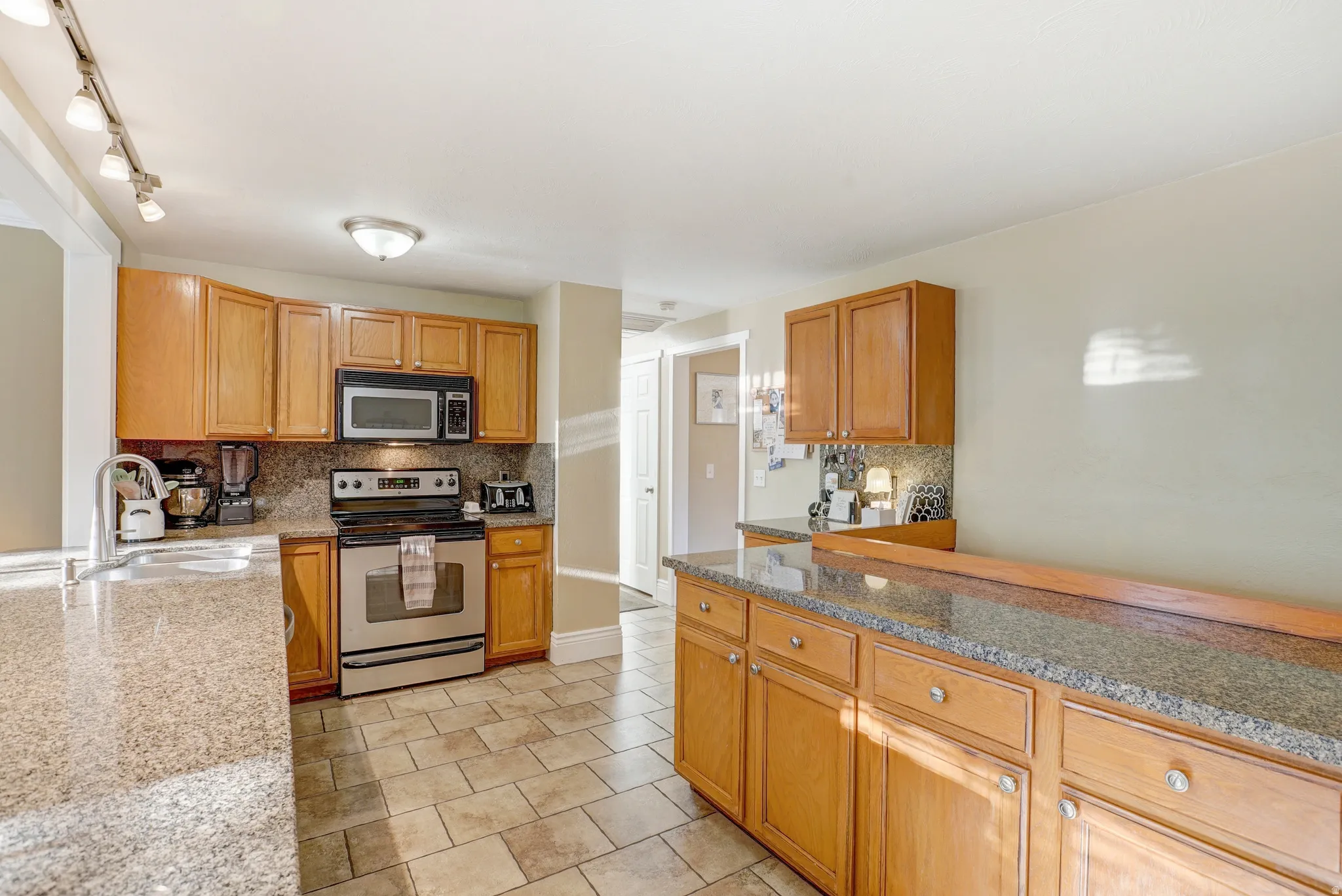 Kitchen featuring tile flooring, wood cabinetry, stone countertops, and stainless steel appliances