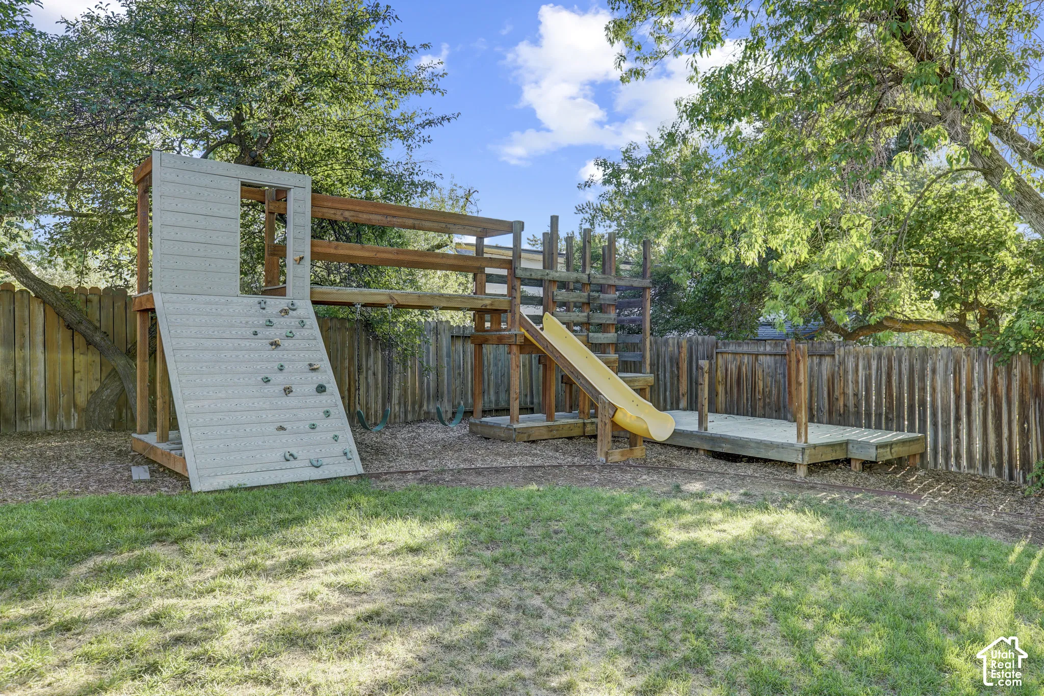 Expansive backyard featuring a wood play structure with a slide, climbing wall, and elevated platform
