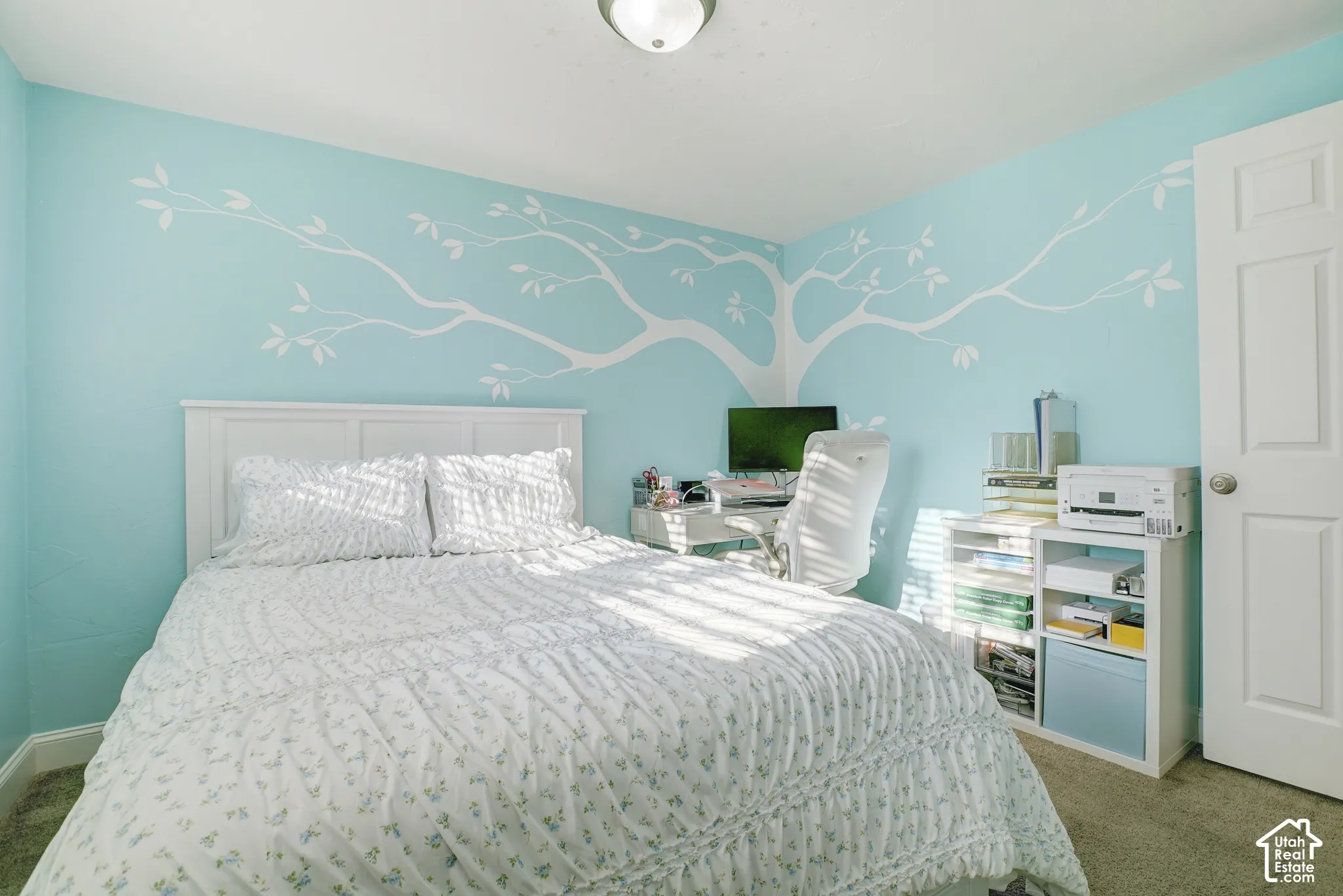 Accent wall with painted tree mural, light blue wall paint, white trim, carpeted flooring, and a white interior door