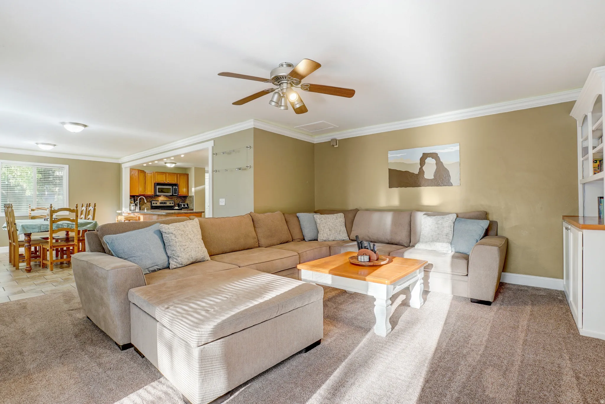 Open-concept living area featuring a ceiling fan, crown molding, and built-in cabinetry with a wood-finish countertop