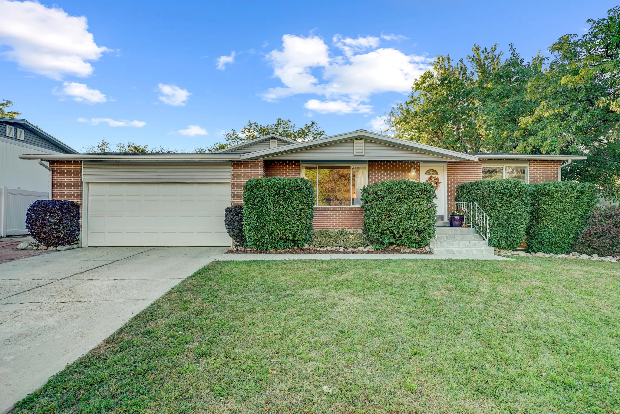 Brick exterior with an attached garage, concrete driveway, and front entryway with steps and a metal handrail