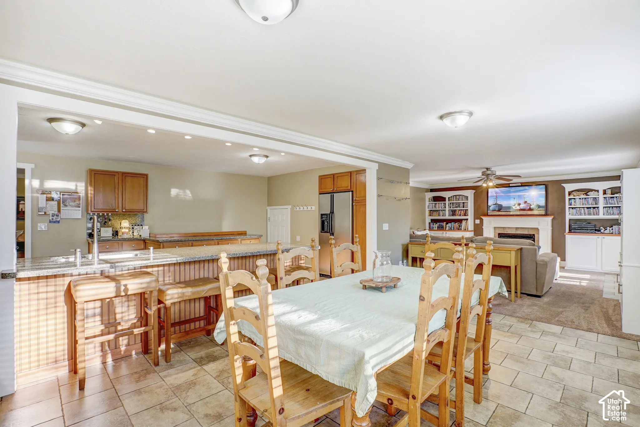 Open-concept layout featuring a kitchen island with seating, a fireplace, ceiling fan, and built-in shelving