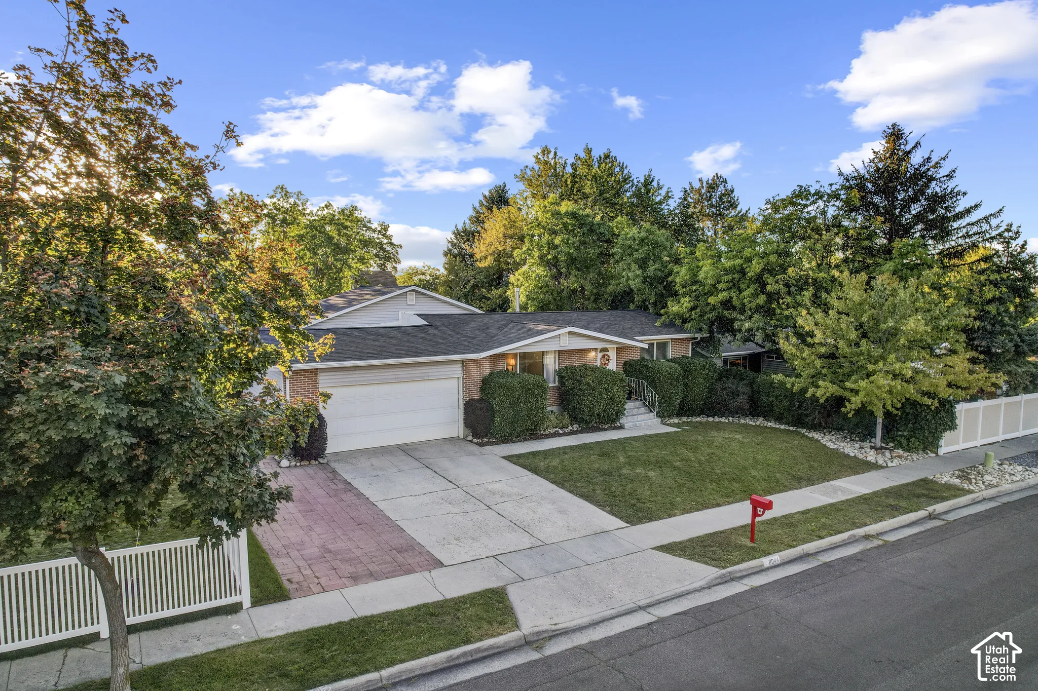 Ranch-style residence featuring a brick facade, attached two-car garage, concrete driveway with brick accents, and a manicured front lawn