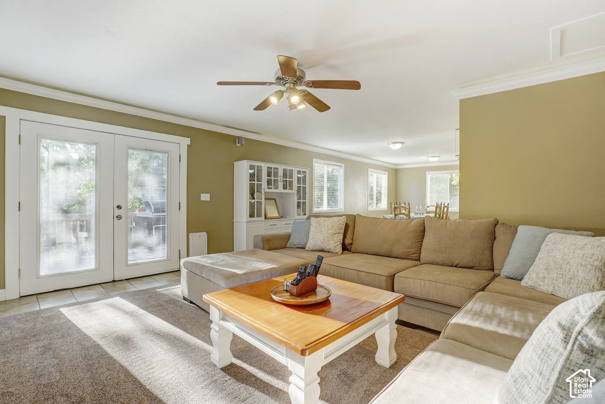 Open-concept living space featuring a ceiling fan, crown molding, and double glass-paneled doors