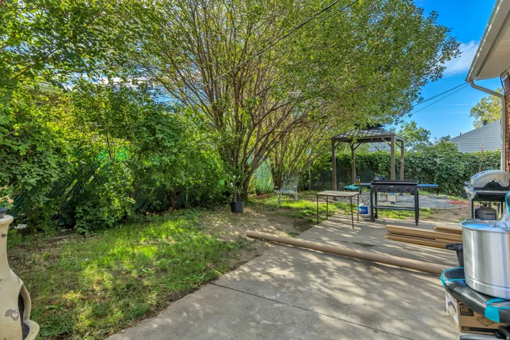 Paved concrete patio area with a wooden gazebo and mature trees providing shade