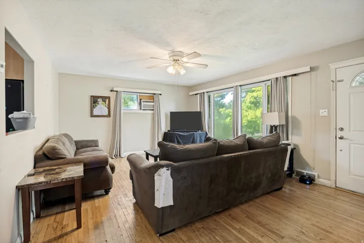 Living area featuring wood-finish flooring, a ceiling fan with integrated lighting, and multiple windows