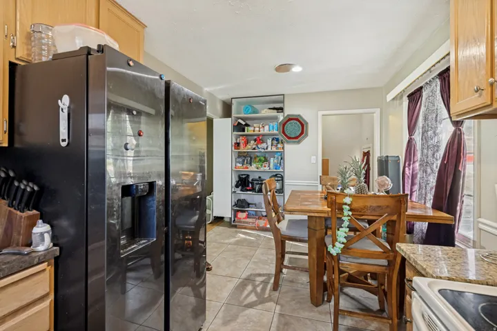 Kitchen featuring wood-finish cabinetry, built-in shelving, tile flooring, and a side-by-side refrigerator with an external dispenser