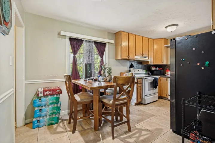 Kitchen with light-toned wood cabinetry, white appliances, and tile flooring
