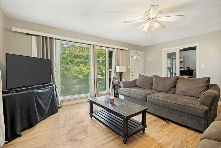 Hardwood-finish flooring, white ceiling fan with integrated lighting, multiple pane windows, and a glass-paneled door