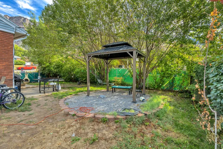 Backyard featuring a gazebo with gravel flooring and a brick-finish border, mature trees providing natural shade, and a brick exterior on the property