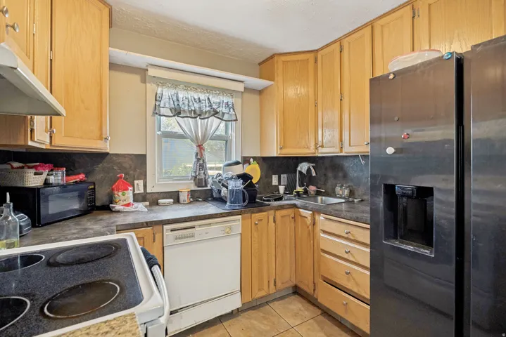 Kitchen featuring wood cabinetry, stainless steel refrigerator, white dishwasher, electric range, and a window above the sink